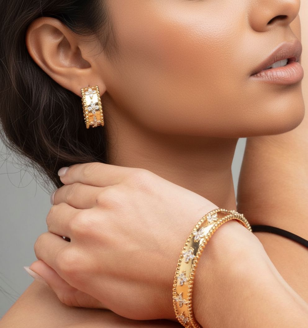 Close-up of a woman wearing gold hoop earrings and bracelet against a neutral background