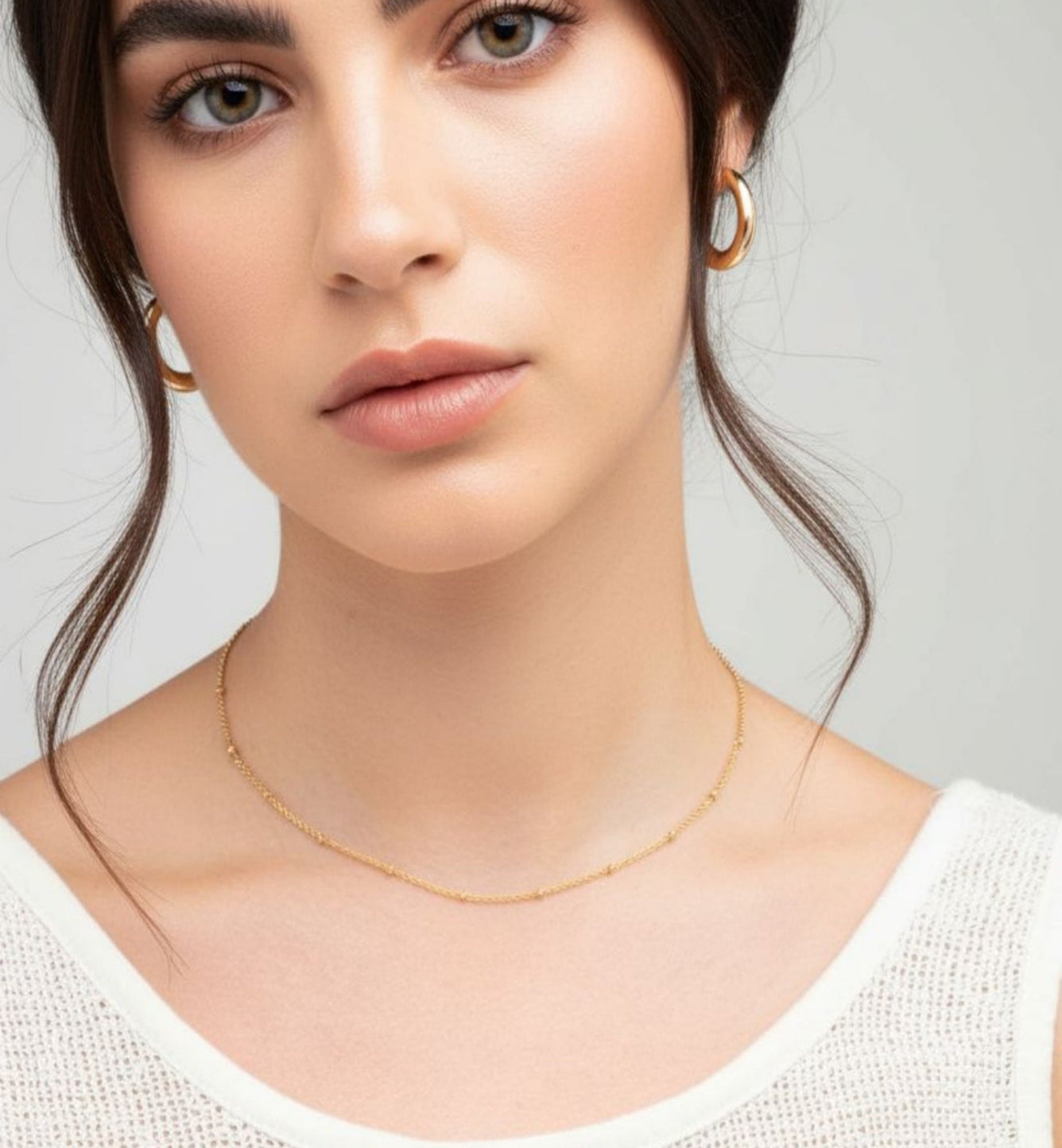 Woman wearing a gold necklace and earrings on a neutral background