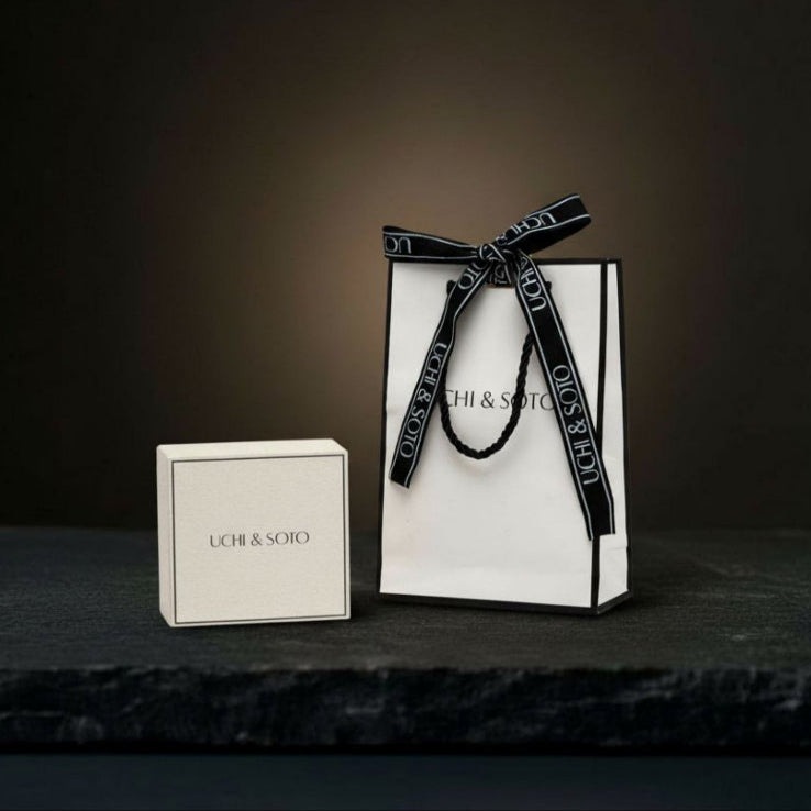 White gift bag with black ribbon and 'Uchi & Soto' branding on a dark surface.