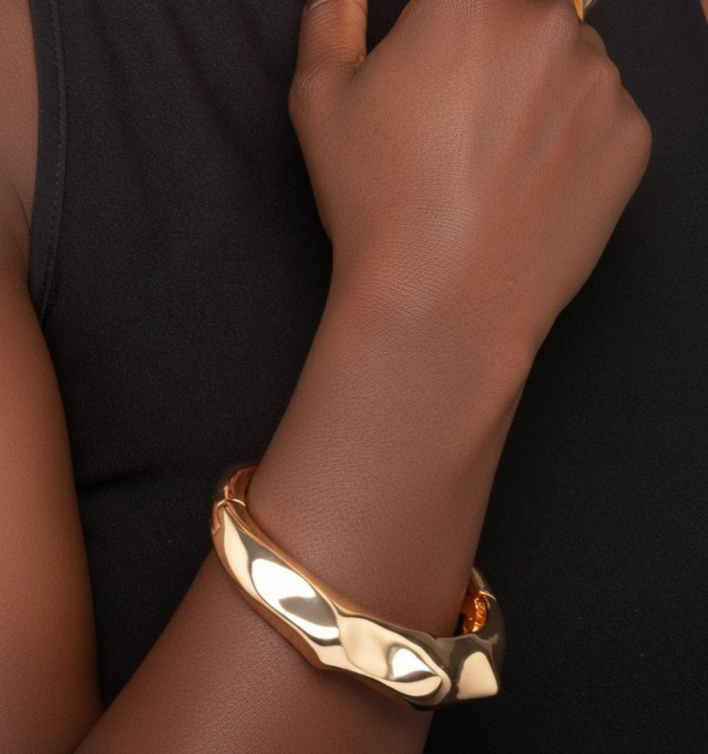 Gold bracelet on a wrist against a black background