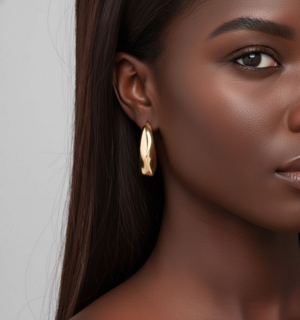 Close-up of a woman wearing gold hoop earrings with a neutral background