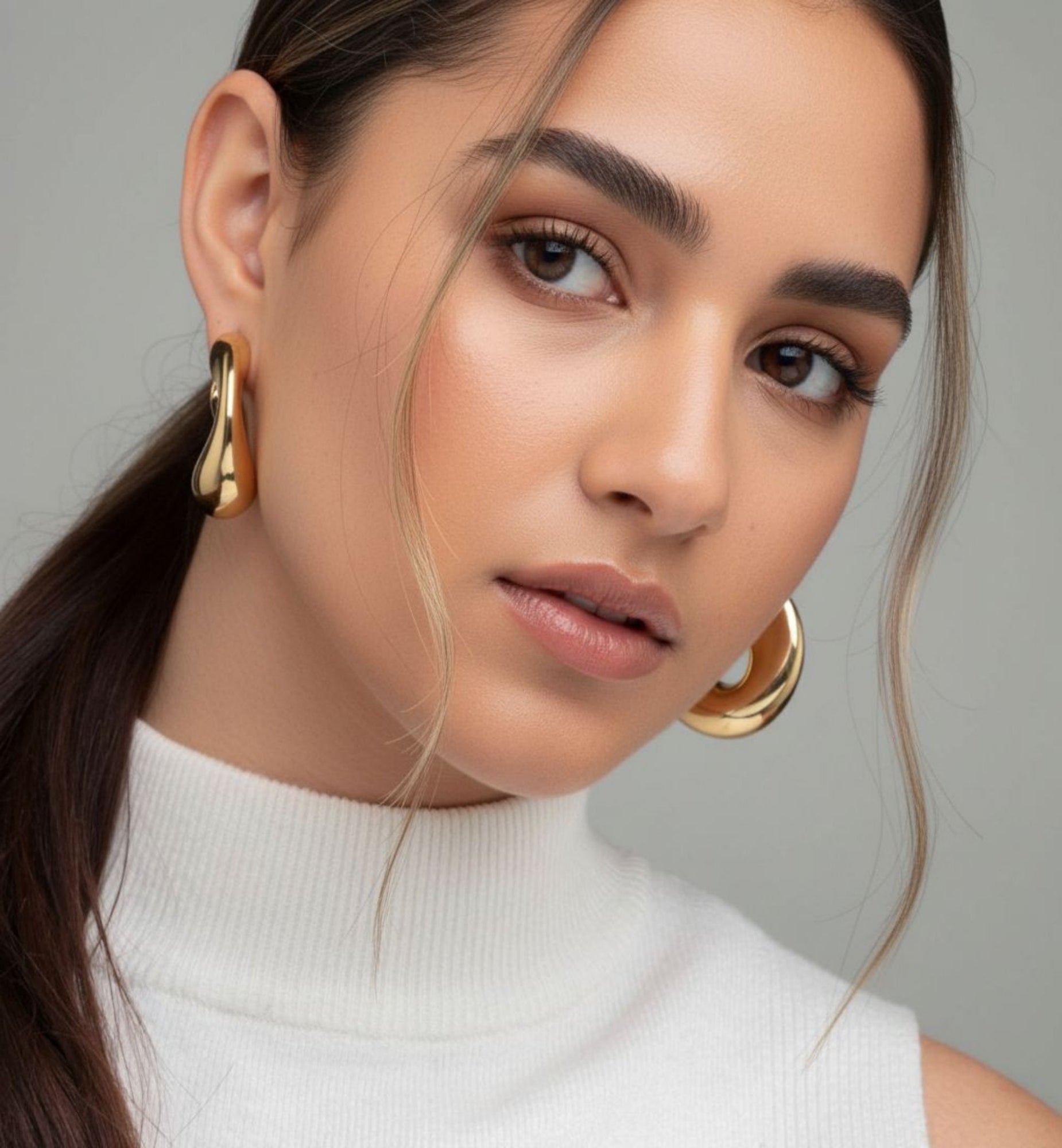 Woman wearing gold hoop earrings with a neutral background