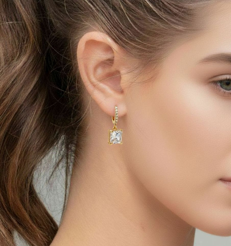 Close-up of a woman wearing a gold earring with a clear gemstone.