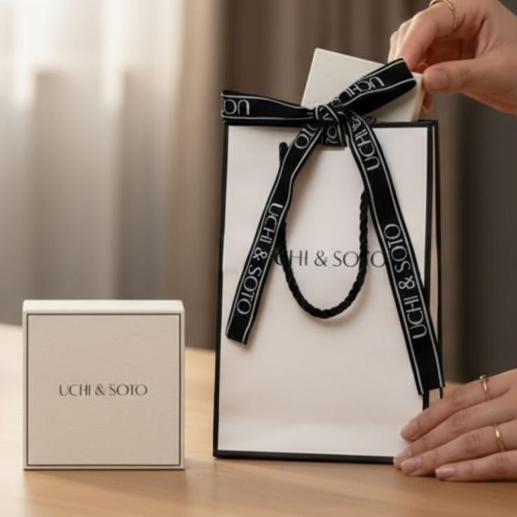 Hand holding a branded gift bag with a box next to it on a wooden surface.