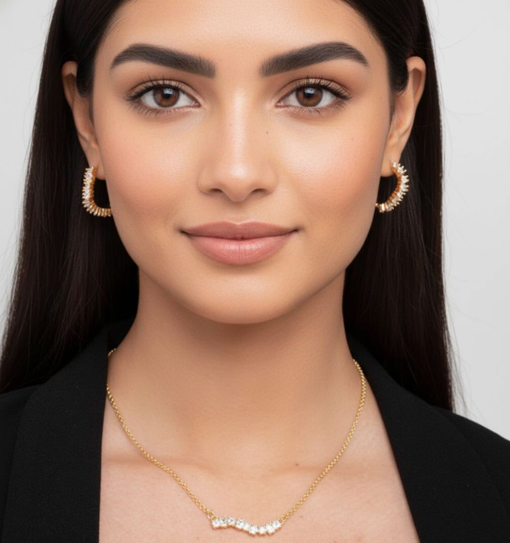 Woman wearing gold earrings and necklace against a white background