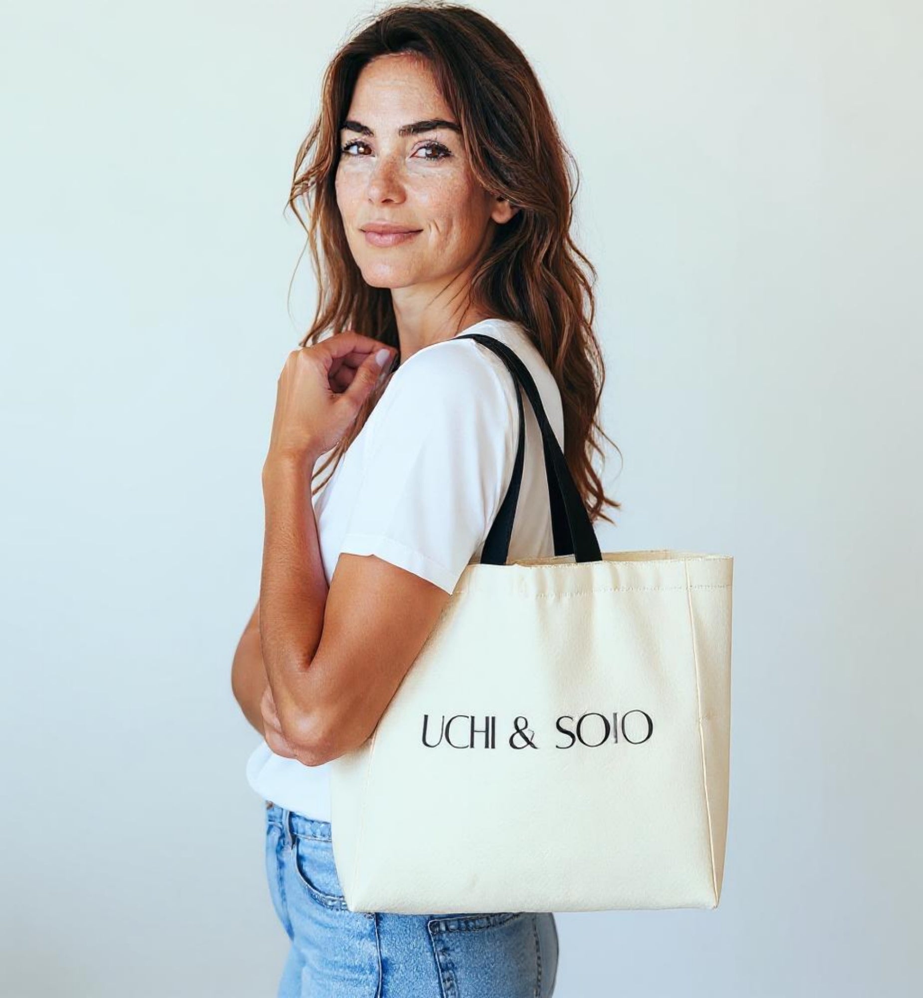 Woman holding a beige tote bag with 'UCHI & SOtO' branding against a light background