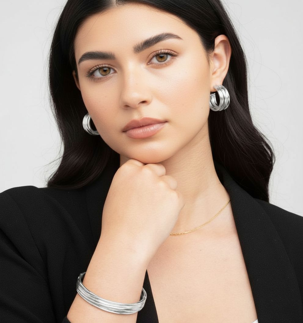 Woman wearing silver hoop earrings and bracelets on a plain background