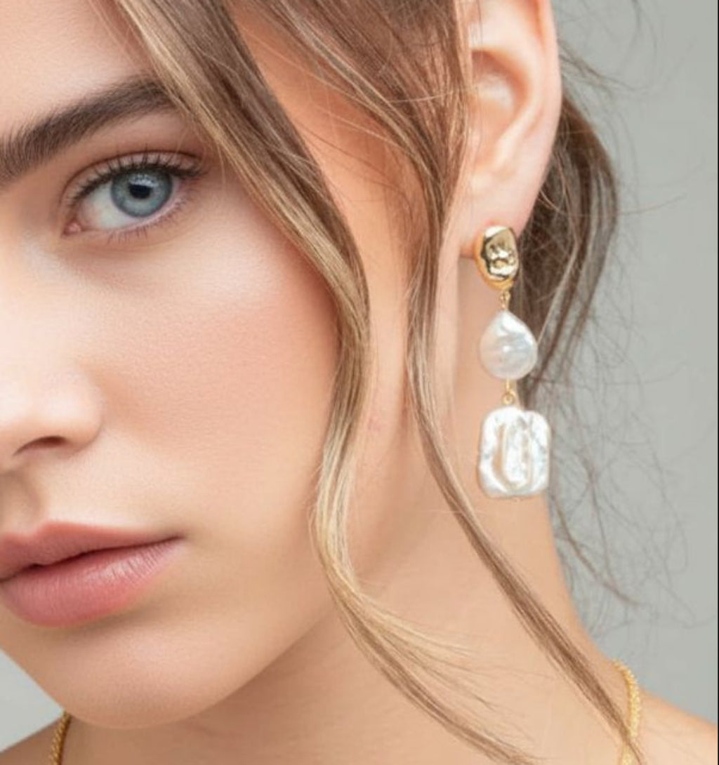 Close-up of a woman wearing gold earrings with pearls against a neutral background