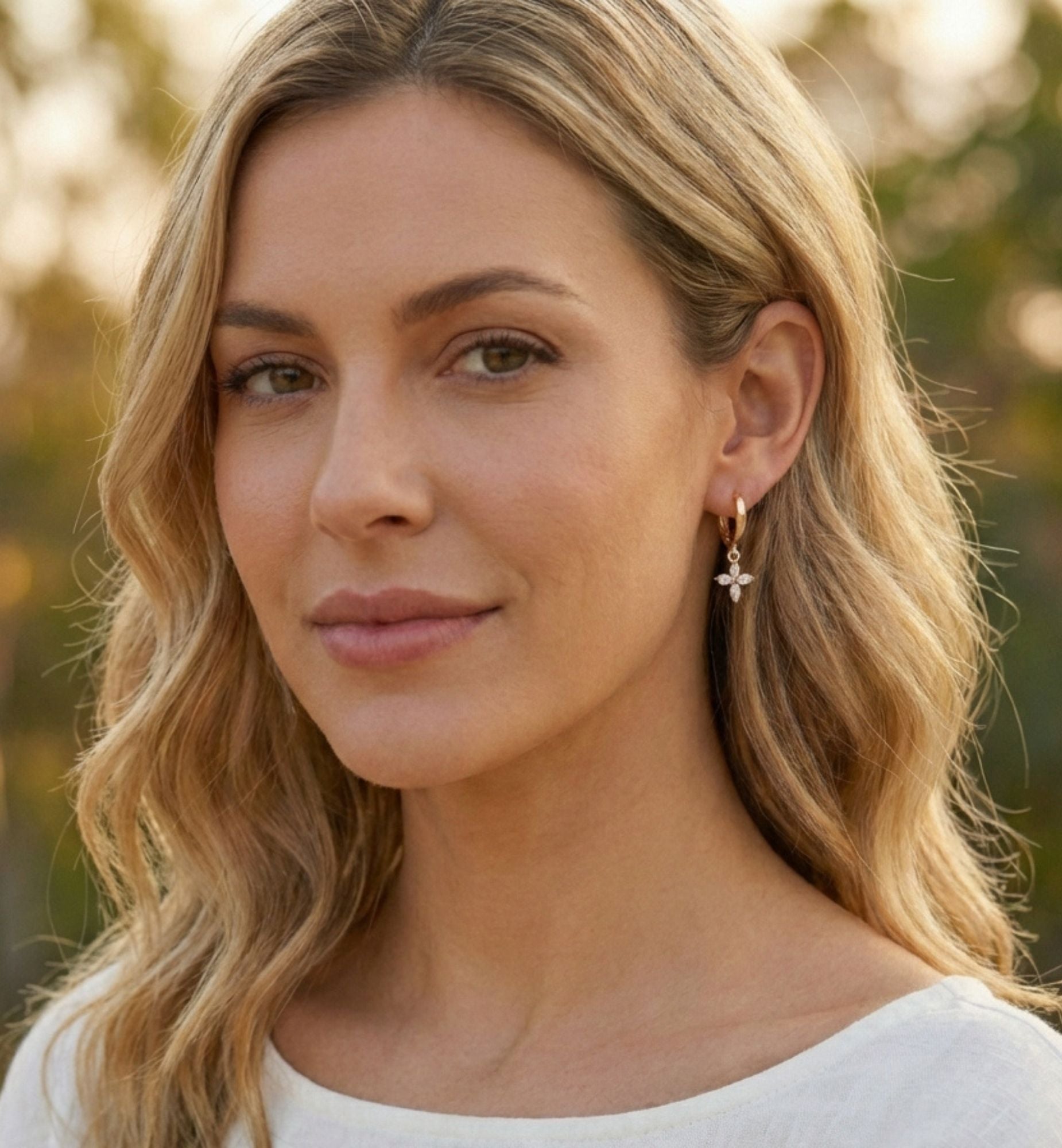 Woman with blonde hair and earrings, wearing a white top, outdoors.