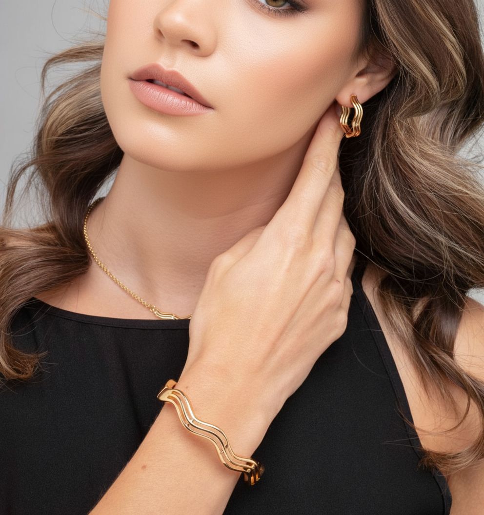 Woman wearing gold jewelry including earrings, necklace, and bracelet against a neutral background