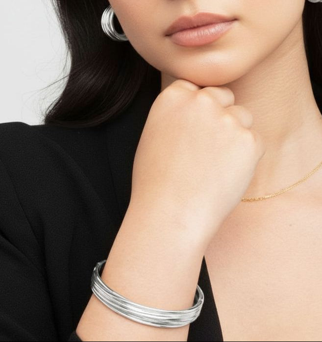 Woman wearing silver hoop earrings and bracelets on a plain background