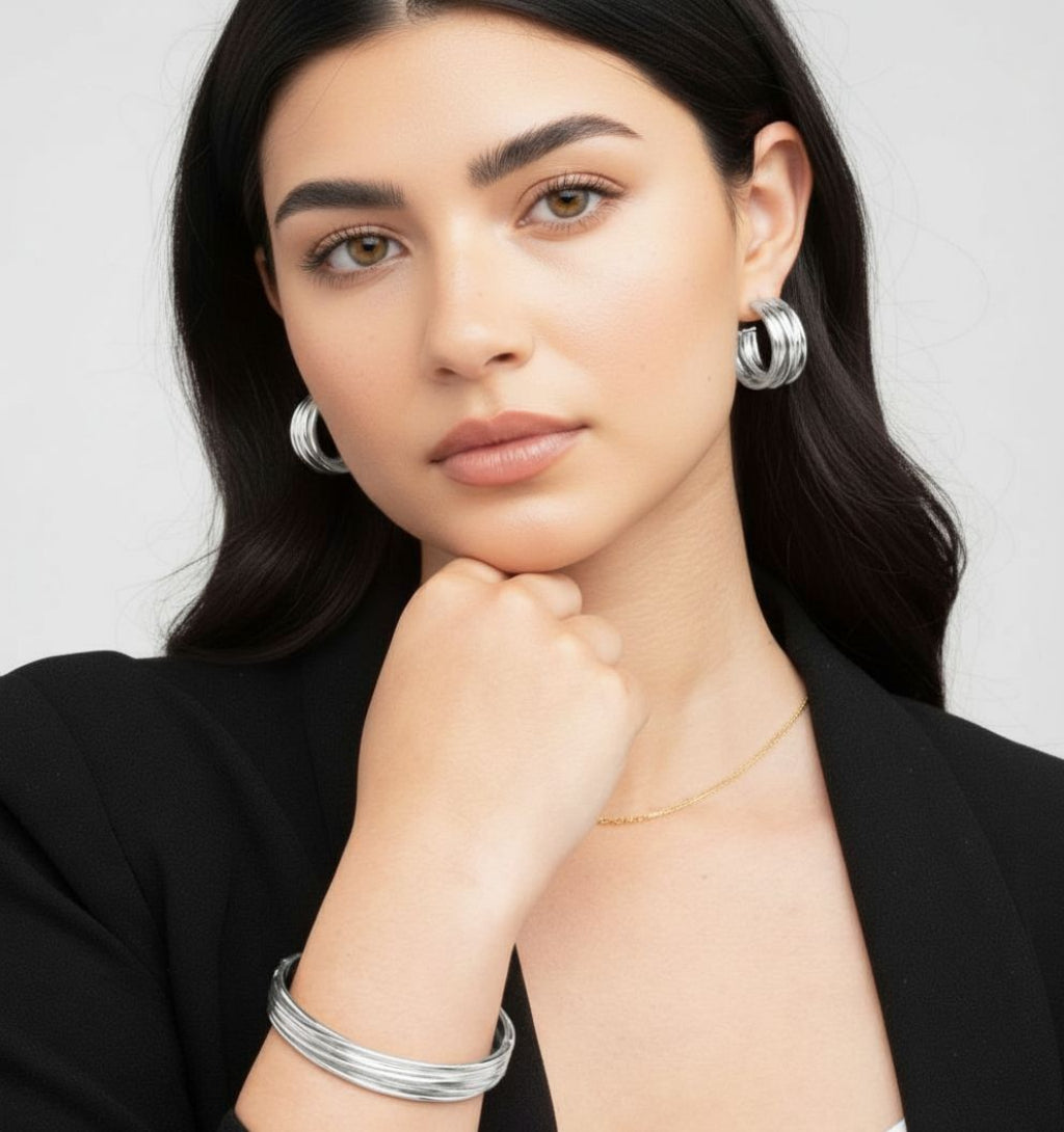 Woman wearing silver hoop earrings and bracelets on a plain background