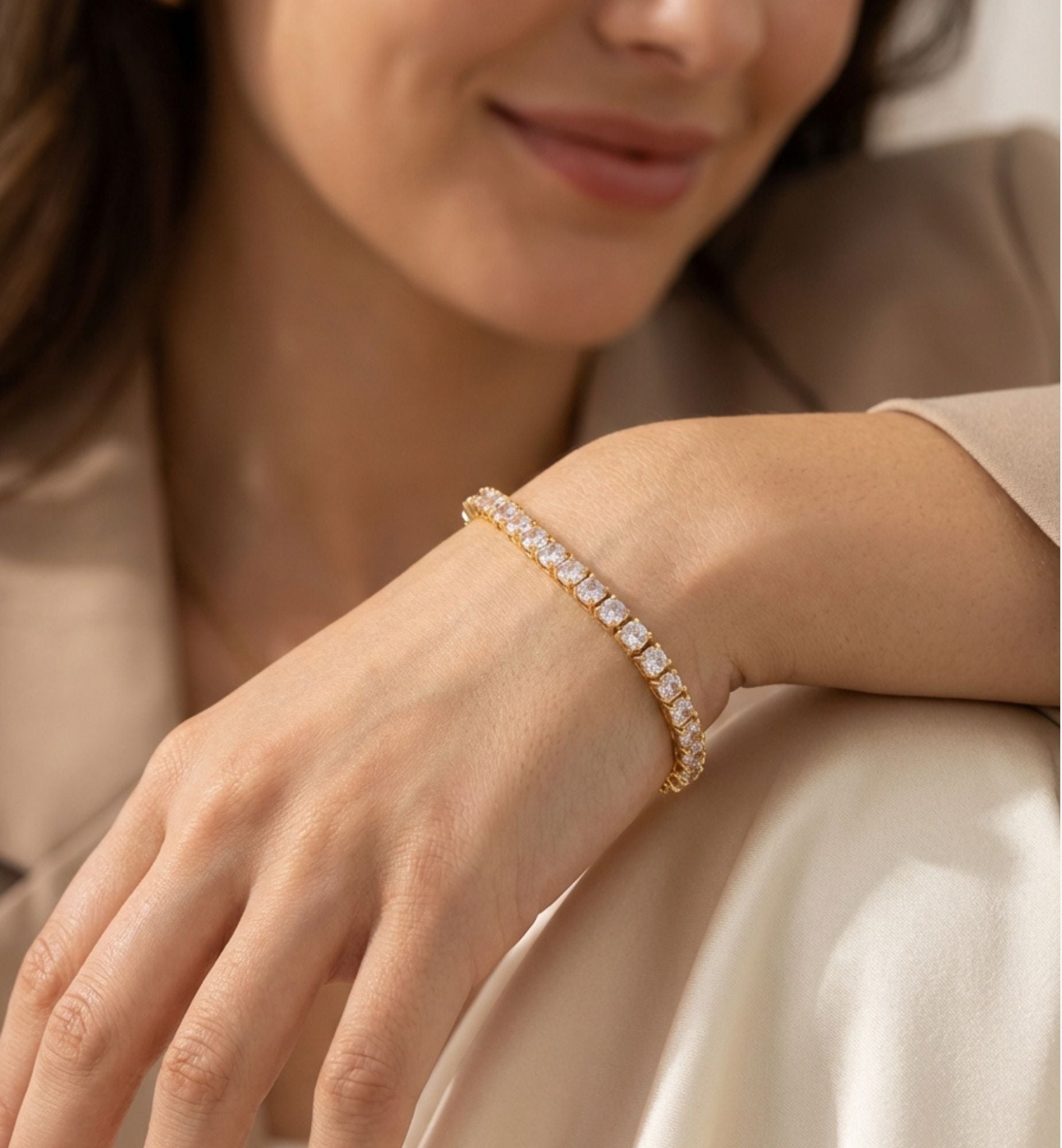Woman wearing a gold bracelet with diamonds on a neutral background